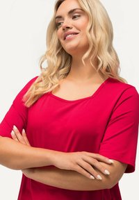 Top corto rosso con scollatura quadrata, realizzato in tessuto morbido. Presenta una vestibilità comoda e una texture liscia, con maniche ripiegate.