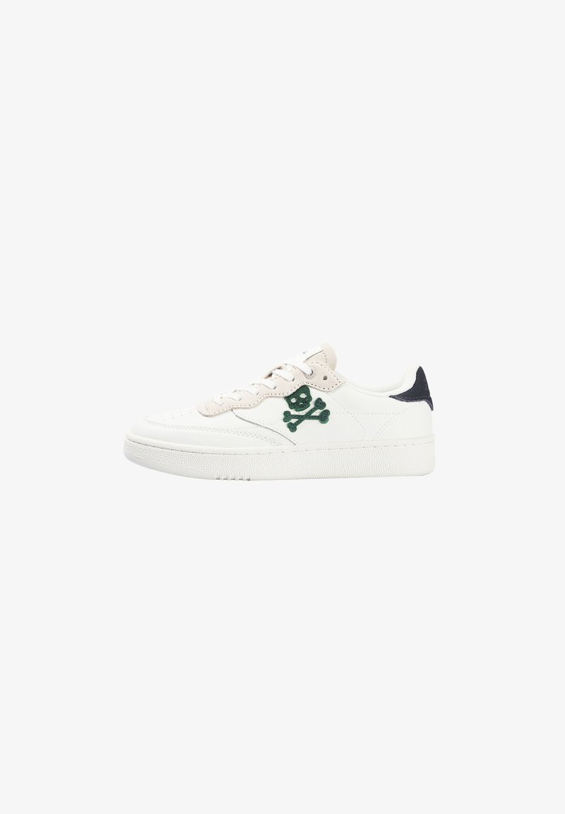 Zapatilla blanca de caña baja con acentos beiges, logo de calavera y tibias verdes en el costado, y detalle negro en el talón.