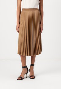 Pleated midi skirt in light brown fabric with a smooth texture and elastic waistband; styled with black ankle strap heels.