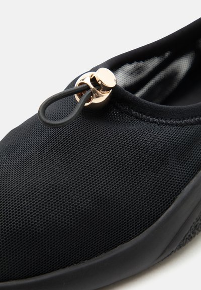 Μαύρο πάνινο slip-on παπούτσι με ελαστική θηλιά και λεπτομέρεια με χρυσό κούμπωμα στο επάνω μέρος, με υφή στη σόλα και επενδεδυμένο γύρω από τον αστράγαλο.