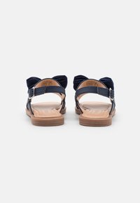 Sandali blu navy con morbidi cinturini in tessuto, chiusura con fibbia regolabile e soletta imbottita color cammello. Suola piatta con dettagli di colore marrone chiaro.