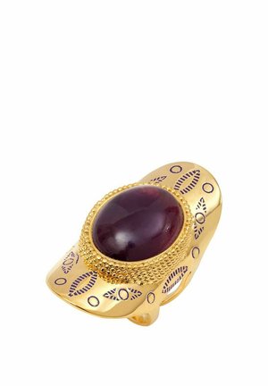 Bague en ton doré ornée d'une pierre ovale rouge foncé, avec des détails texturés et des accents gravés dans un motif répétitif le long de l'anneau.