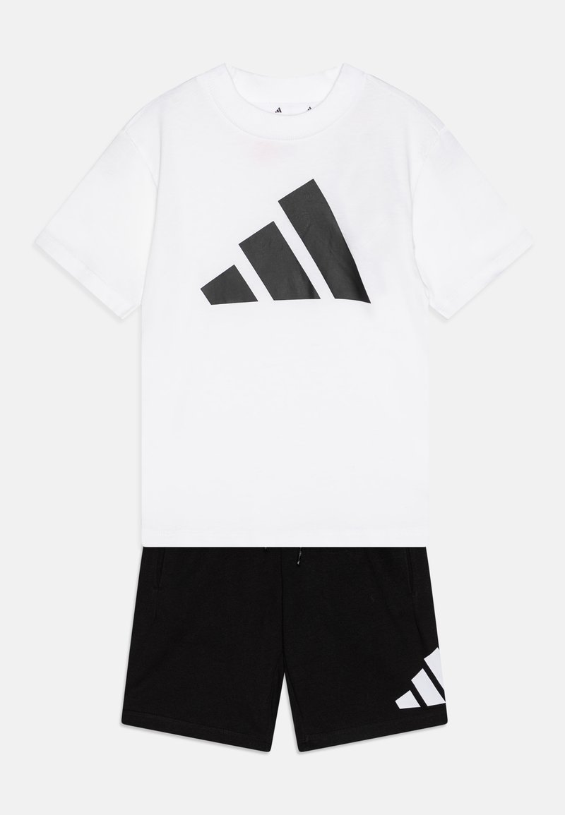 Camiseta de algodón blanca con un gran logotipo negro de Adidas. Combinada con pantalones cortos negros, que presentan un detalle de franja blanca en el costado.