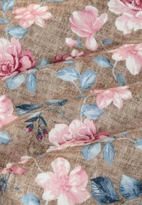 Bloemenstof met roze en blauwe bloemen op een bruine, gestructureerde achtergrond, met zichtbare plooien en een zachte, geweven textuur.