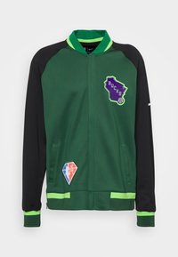 Chaqueta verde y negra con cierre frontal, que presenta el logo "BUCKS", parches coloridos y franjas verdes en el cuello y los puños.