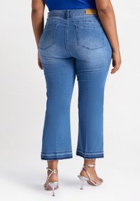 Helle blaue Jeans mit weitem Beinausschnitt, fransigen Säumen, fünf Taschen und hohem Bund, kombiniert mit metallischen Absatzsandalen.