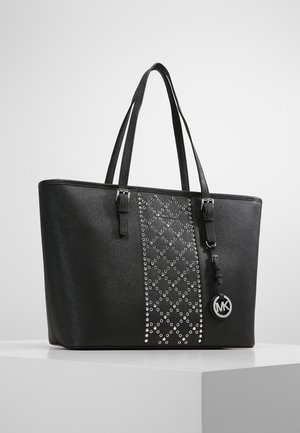 Black tote bag with two shoulder straps, central panel of silver studs in diamond pattern, and round MK logo charm hanging from strap.