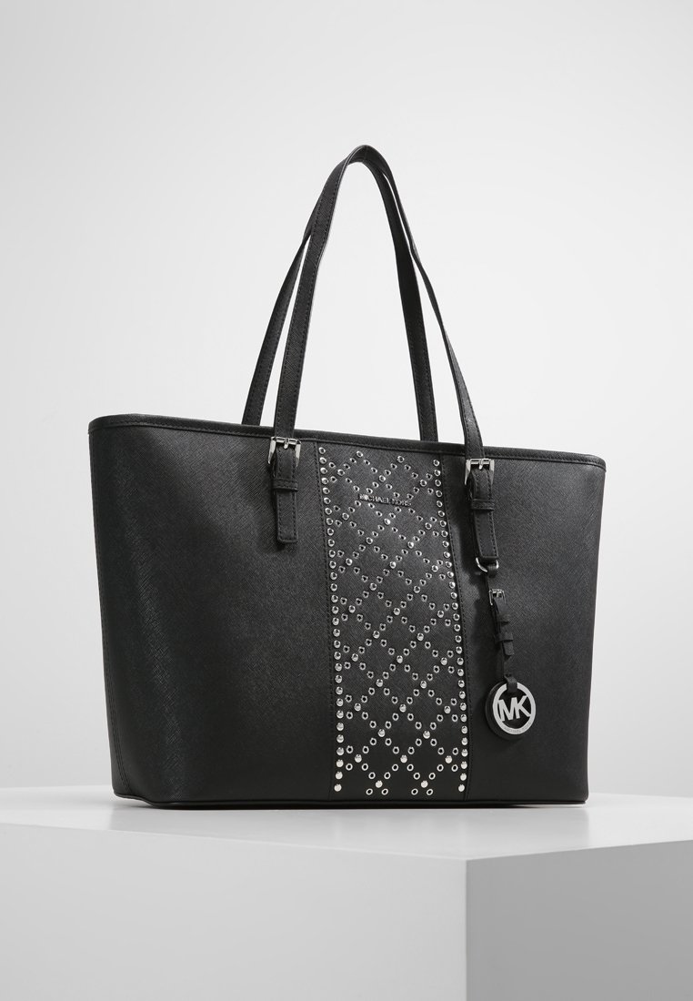 Sac cabas noir avec deux bretelles, panneau central clouté en argent au motif losange, et pendentif rond avec le logo MK suspendu à la sangle.