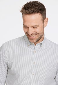Camisa de botones a rayas en gris claro y blanco, con cuello, bolsillo en el pecho y textura ligera. Los botones son de tamaño mediano y de color claro.