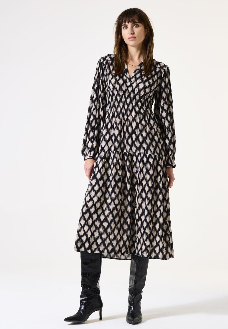 Robe longue à motifs noirs et crème avec une taille plissée, des manches longues et une jupe à volants ; assortie à des bottes noires à talons.
