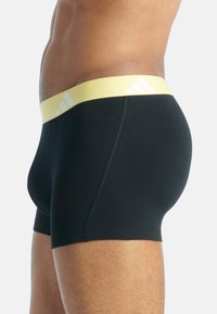 Schwarze Boxershorts mit einem gelben elastischen Bund und weißem Branding. Glattes Material, taillierte Form und mit Flachnähten für zusätzlichen Komfort.