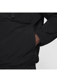 Černá lehká bunda s elastickými manžetami a přední kapsou. Tkanina je hladká, má minimalistický design a není na ní žádné viditelné logo.