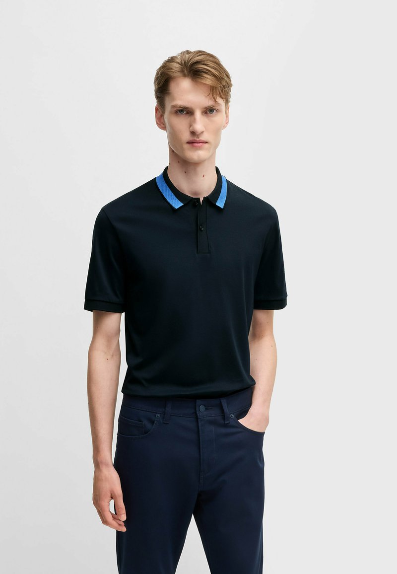 Svart polotröja med blå krage, korta ärmar och knapplist. Matchad med mörkblå byxor. Slät tygtextur.