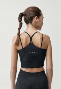 Čierna športová podprsenka s priliehavým strihom, žebrovanou textúrou a nastaviteľnými tenkými ramienkami. Na chrbte je umiestnené logo, v kombinácii s vysokými legínami.