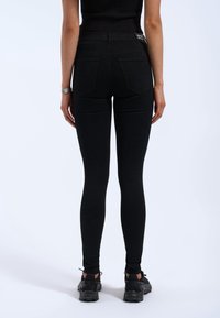 Svarta högmidjade jeans med en åtsittande silhuett, med två bakfickor och en slät textur. Bärs med svarta skor.