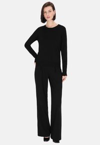 Zwarte lange mouwen trui en wijde broek. De outfit heeft een zachte textuur en een klassieke ronde halslijn, wat zorgt voor een minimalistische uitstraling.