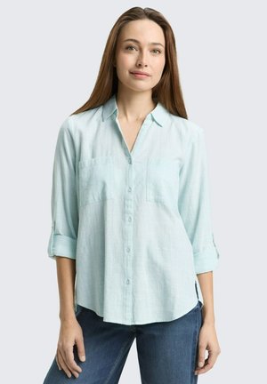 Camicia azzurro chiaro con bottoni, due tasche sul petto, maniche lunghe arrotolate e vestibilità ampia. Realizzata in un tessuto strutturato e traspirante.