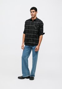 Camisa xadrez preta e cinza com gola abotoada, mangas compridas e bolso no peito, combinada com jeans de perna larga azul claro e botas pretas.