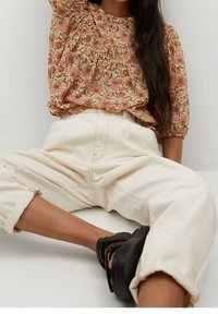 Blumenbluse mit kurzen Puffärmeln in Beige- und Rosatönen, kombiniert mit lässigen, cremefarbenen Hosen mit umgeschlagenen Säumen und schwarzen Sandalen.