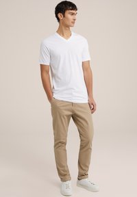 Witte v-hals t-shirt gecombineerd met kaki broek en witte sneakers. Het shirt heeft korte mouwen en is gemaakt van een gladde, lichte stof.