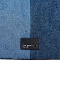 Δύο τόνων γαλάζιο τζιν ύφασμα με μια μαύρη ετικέτα που αναγράφει "KARL LAGERFELD JEANS" στο κέντρο του πάτου.