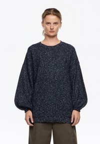 Granatowy sweter o ziarnistej fakturze, z balonowymi rękawami i okrągłym dekoltem, wykonany z miękkiego, grubego dzianiny.