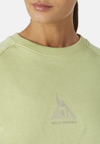 Sudadera verde claro con cuello redondo, puños acanalados y un sutil logotipo bordado de una casa con chimenea en el pecho.