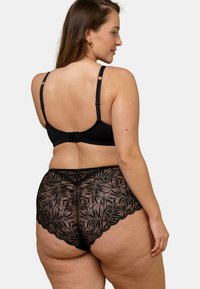Sous-vêtements en dentelle noire avec des motifs floraux, présentant des bords festonnés et une taille lisse. Les bretelles réglables du soutien-gorge noir complètent le design.