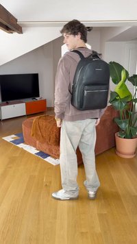 Rucsac negru din piele cu suprafață texturată, mânere superioare, curele reglabile și buzunar frontal cu fermoar, purtat de o persoană îmbrăcată casual.