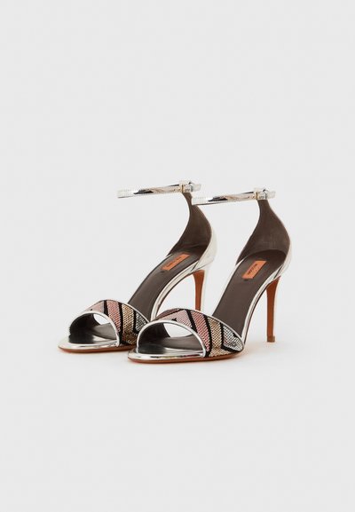 Pantofi cu toc înalt, cu vârful deschis, având o curea strălucitoare pentru gleznă din argint, un material superior multicolor cu paiete metalizate în modele geometrice și o branț maro.