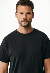 Černé bavlněné tričko s kulatým výstřihem, krátkými rukávy a nenápadným logem na hrudi. Hladká textura, volný střih.