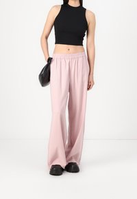Černý bezramínkový crop top v kombinaci se světle růžovými širokými kalhotami s elastickým pasem. Modelka nese černou zaoblenou kabelku.