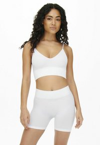 Hvid ribbet crop top med tynde stropper parret med højtaljede hvide shorts. Glat tekstur, tætsiddende design og minimalistisk stil.