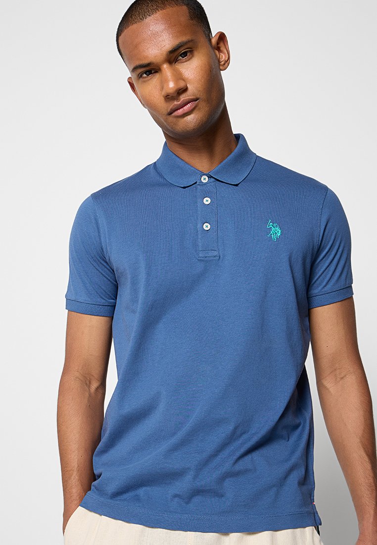 Blaues Poloshirt aus Baumwolle mit gerippter Textur, ausgestattet mit einer Knopfleiste mit drei Knöpfen und einem kleinen gestickten Logo in Grün auf der Brust.