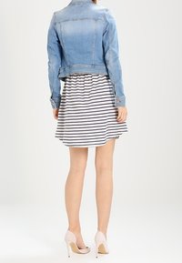 Jasnoniebieska kurtka dżinsowa o skróconym kroju, zestawiona z białą sukienką w granatowe paski. Miękkie tkaniny i różowe buty na wysokim obcasie.