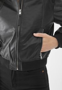 Giubbotto bomber in pelle nera con chiusura a zip, polsini e orlo a costine; presenta tasche laterali con zip e texture liscia.