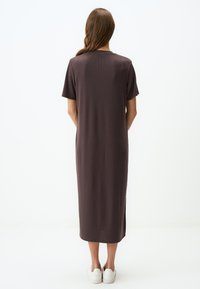 Robe marron mi-longue avec manches courtes, texture côtelée, fentes latérales et coupe décontractée, associée à des baskets blanches.