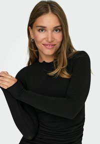 Top negro de manga larga con cuello redondo y textura acanalada. Cuenta con mangas ajustadas y un ligero fruncido a lo largo del costado para un aspecto estilizado.