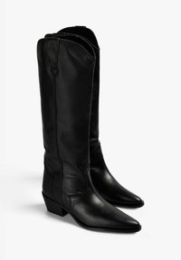 Botas de cuero negro hasta la rodilla con punta afilada y tacón cuadrado, que cuentan con costuras verticales y una apertura flexible en la parte superior.
