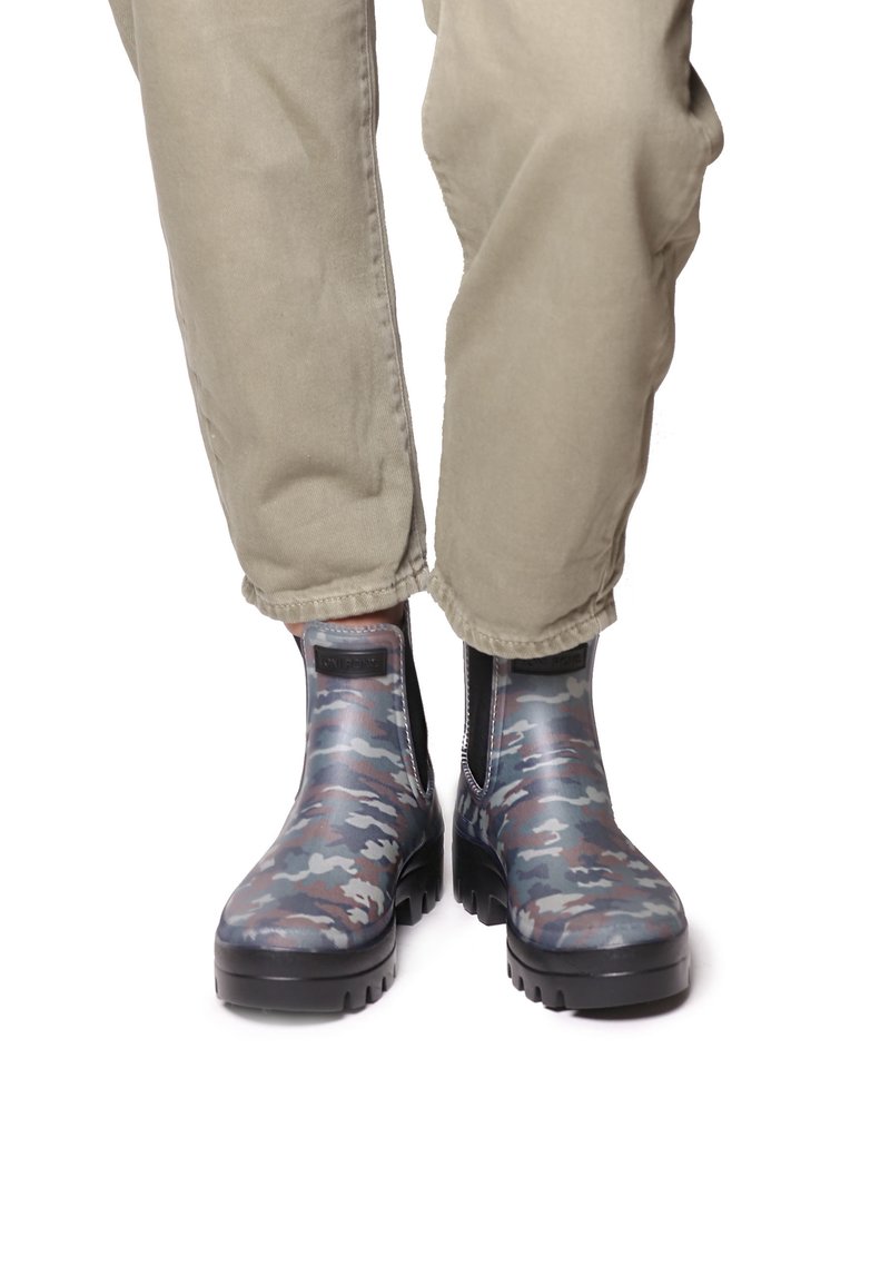 Kumipohjaiset nilkkasaappaat sinivihreässä ja harmaassa kamouflagekuviossa, joissa on teksturoitu pinta, elastiset sivupaneelit ja paksu musta pohja.