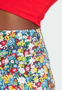 Pantalones cortos de talle alto con estampado floral sobre un fondo azul. Presentan flores rojas, amarillas y blancas. Logo de Adidas bordado en la cinturilla.