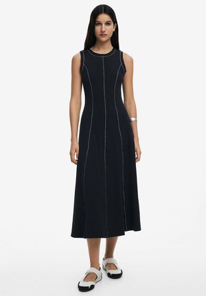 Schwarzes ärmelloses Kleid mit tailliertem Oberteil, schwingendem, knöchellangem Saum, kontrastierenden weißen Nähten und glatter Baumwolltextur.