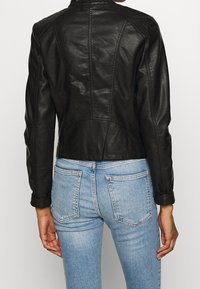 Giacca in pelle nera con una silhouette aderente, spalle texturizzate e dettagli sui cuciture. Abbinata a jeans aderenti di colore azzurro chiaro.