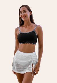 Černý crop top s vzorovanými pásky a bílou zúženou sukni s krajkovými detaily a nastavitelnou šňůrkou. Hladké textury a přiléhavé střihy.