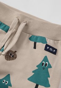 Beige katoenen joggers met turkooizen patronen van bomen en eikels, een taille met trekkoord en een P.O.P.-label. Zachte textuur en speelse ontwerpen.