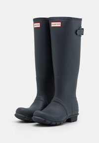 Botas de lluvia de goma negras con acabado mate, parte superior curvada y tacón cuadrado. Incluyen hebilla lateral y etiqueta de logo roja. Suela texturizada para agarre.