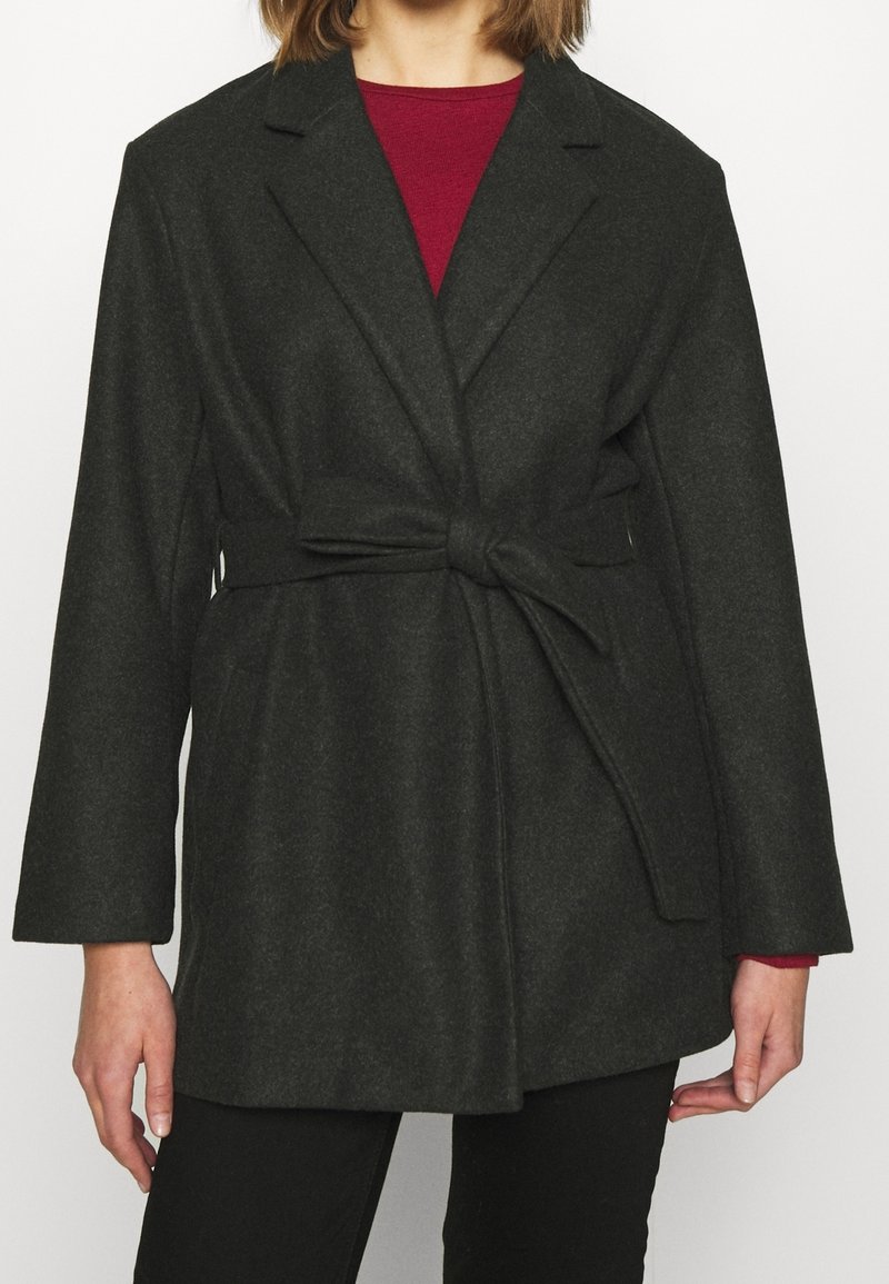 Cappotto in misto lana grigio scuro con design avvolgente, caratterizzato da una vita con cintura, rever a punta e maniche lunghe. Texture liscia e dettagli minimi.