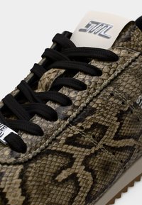 Gros plan sur une chaussure de sport avec des lacets noirs et une tige en cuir à imprimé serpent texturé dans des tons marron et beige.