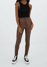 Bruine nep leren high-waisted skinny broek gecombineerd met een zwarte geribbelde mouwloze top en zwart-witte platformsneakers.