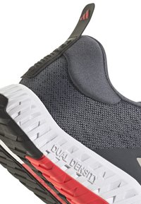 Gray athletic shoe featuring a textured mesh upper, black accents, and a dual-density sole with red detailing. Pull tab on heel.